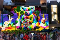 Vibrant pop-surrealism style mural lit up at night featuring Australian flora and fauna